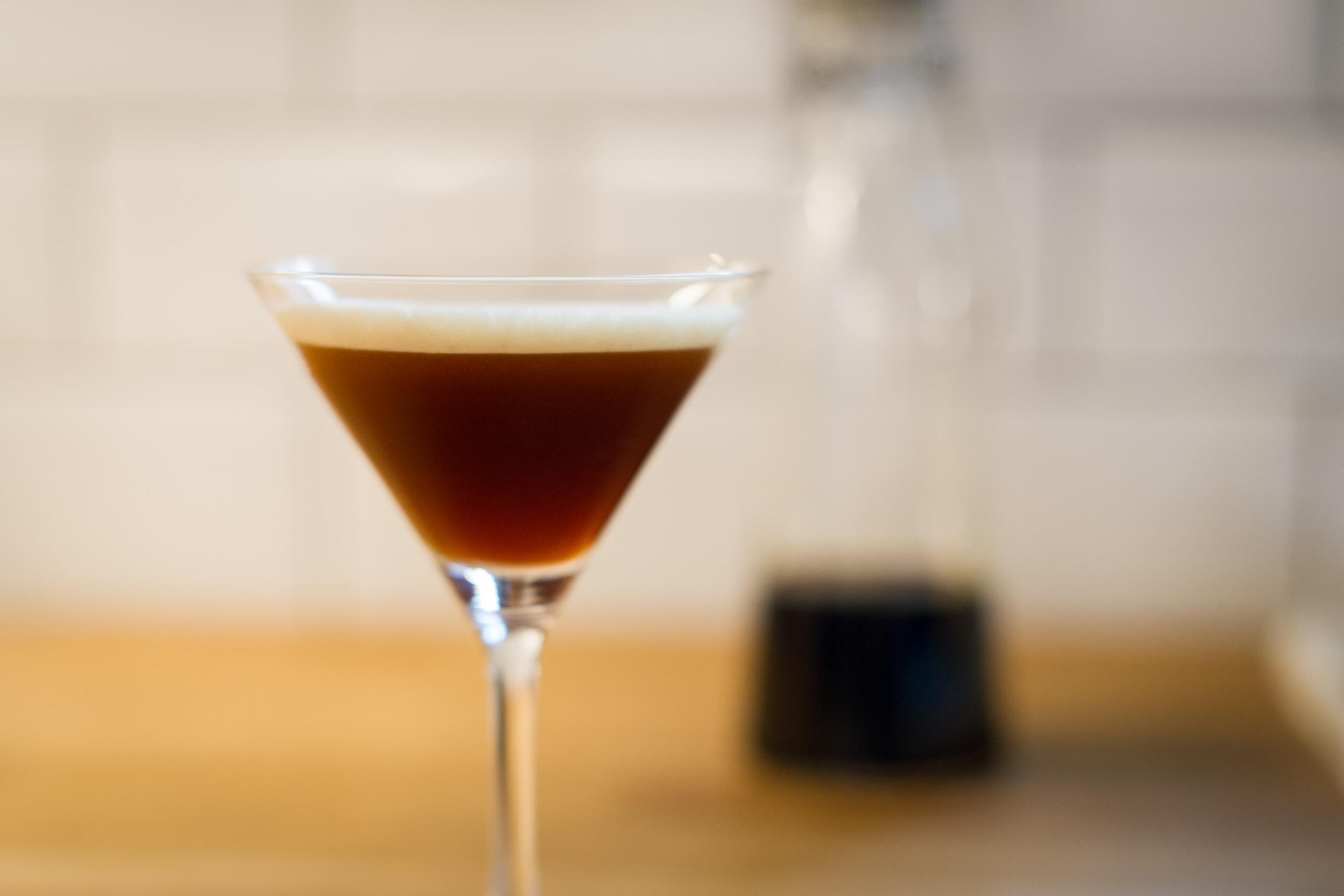 a cocktail glass with espresso martini and liquor in the background