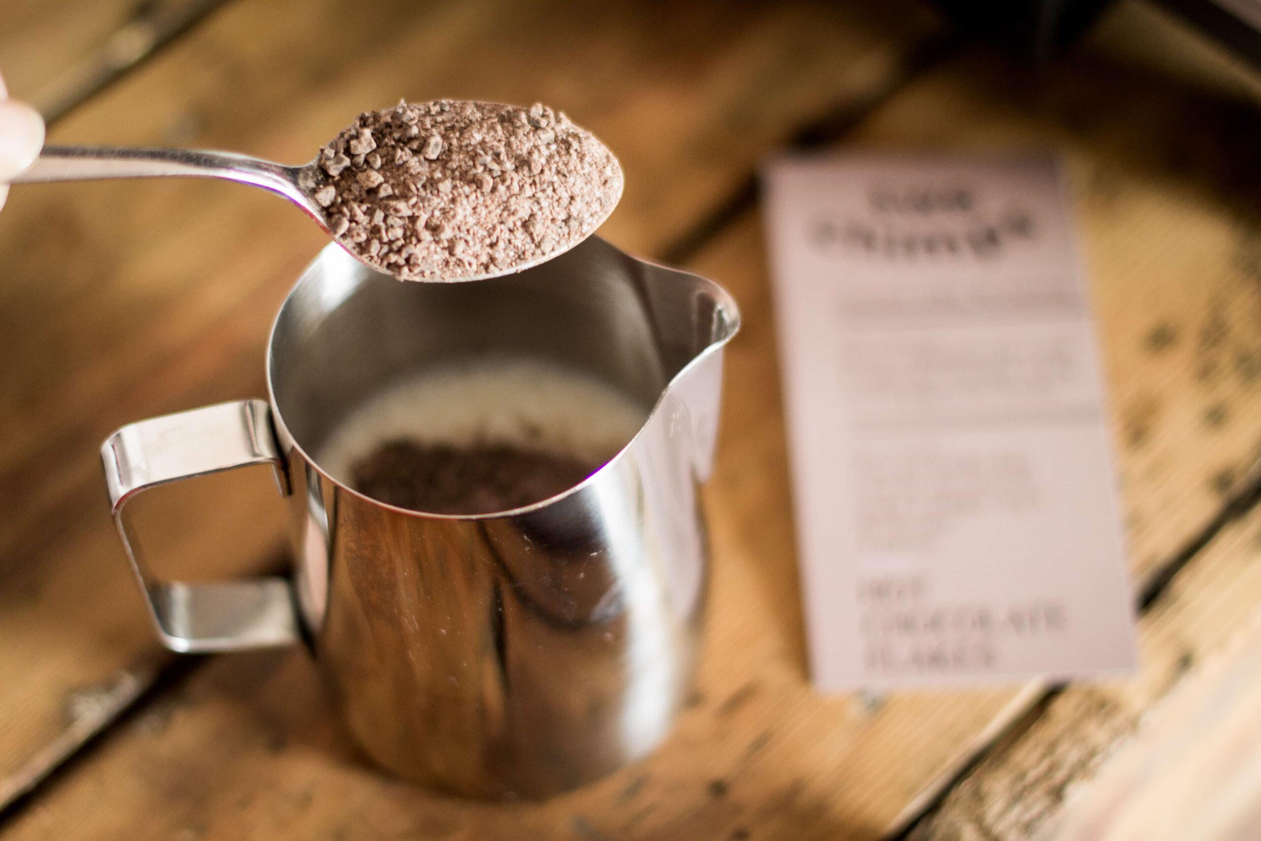 spoon full of hot chocolate flakes over a metal jug of milk