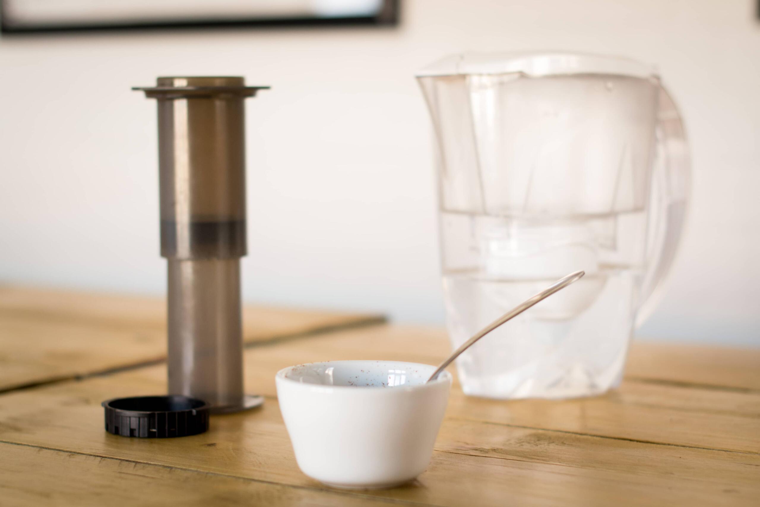 Brita water filter on a table with AeroPress and white bowl of coffee 
