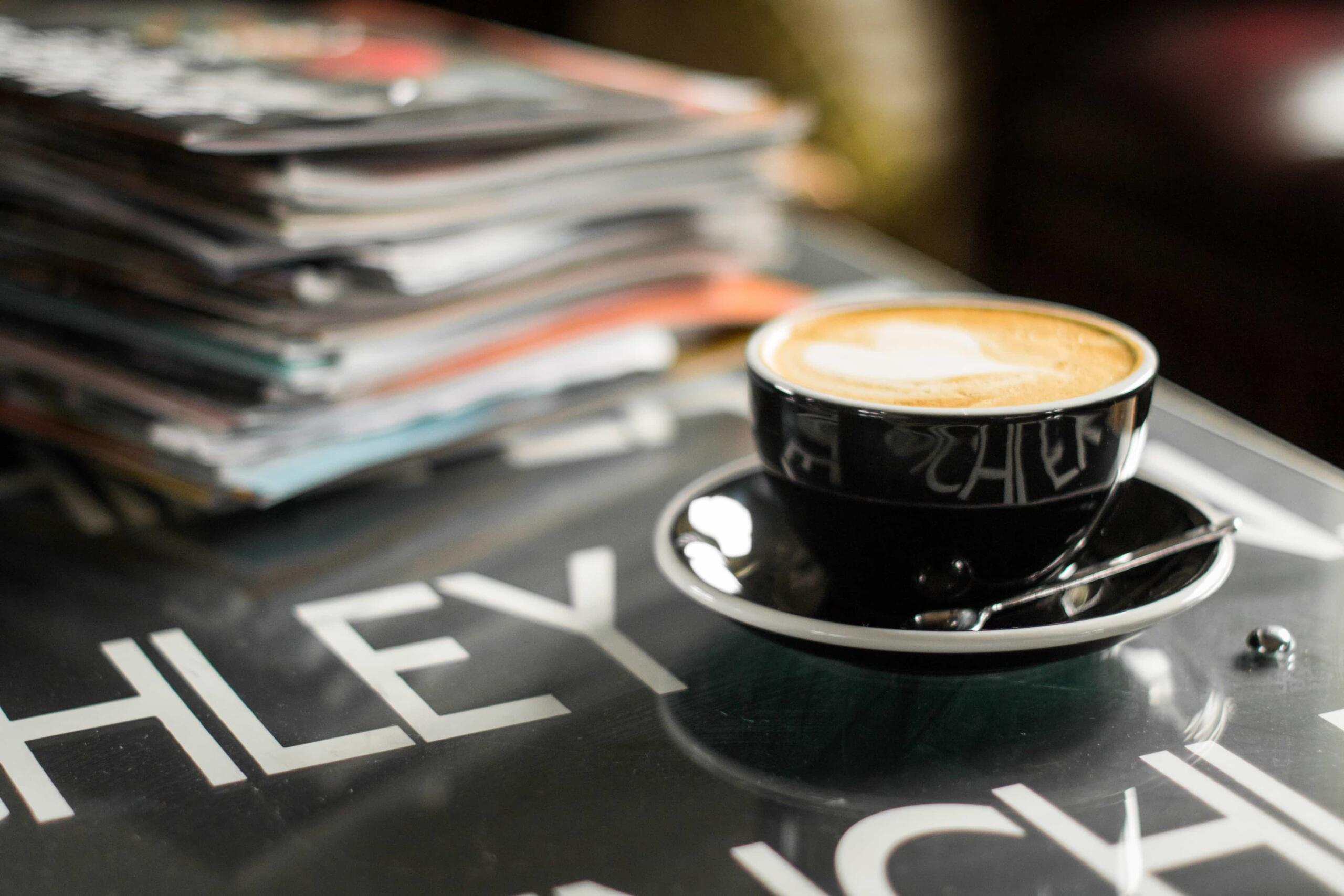 Latte in a black cup with stack of magazines