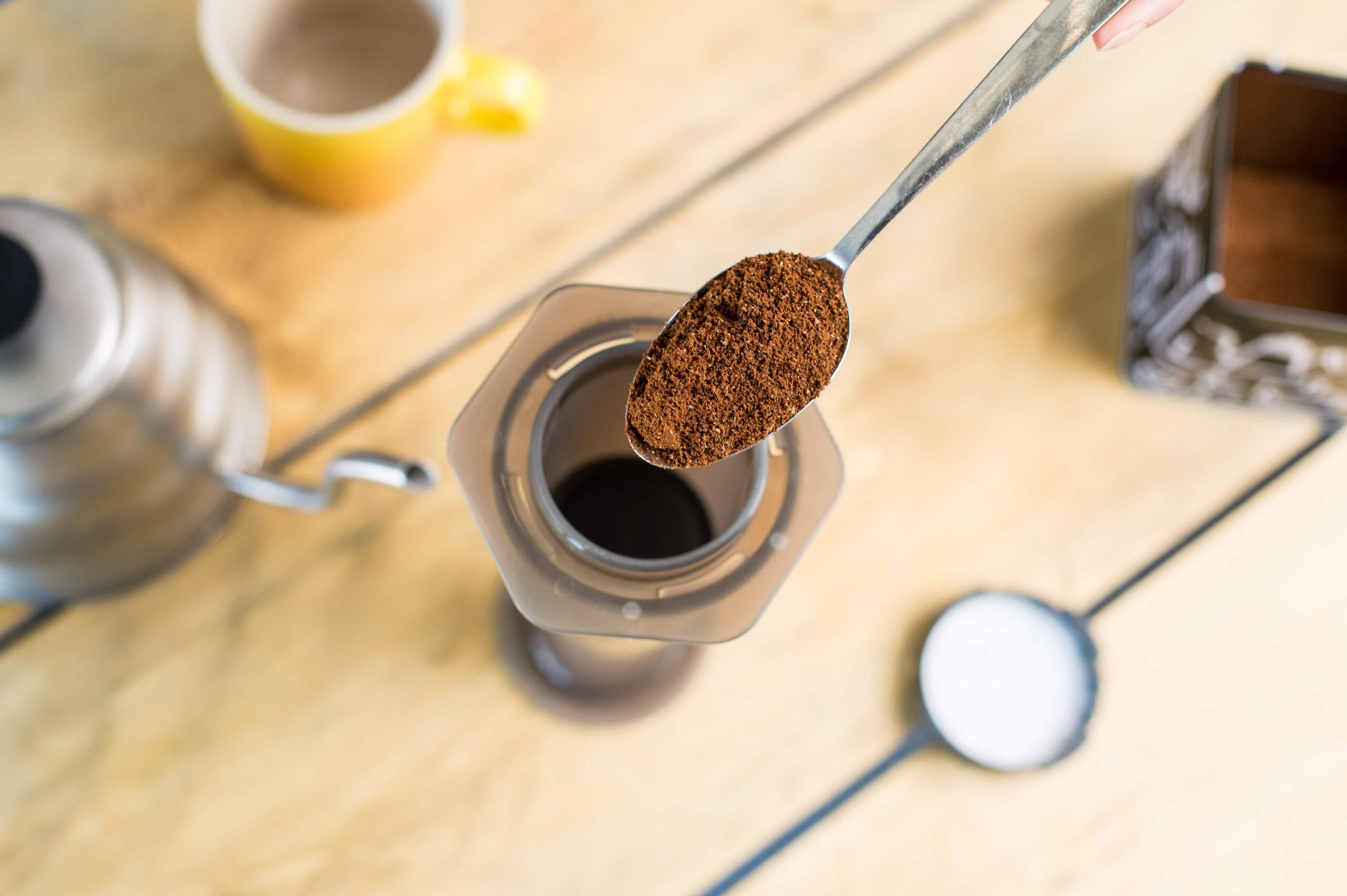 tipping ground coffee into AeroPress using a spoon