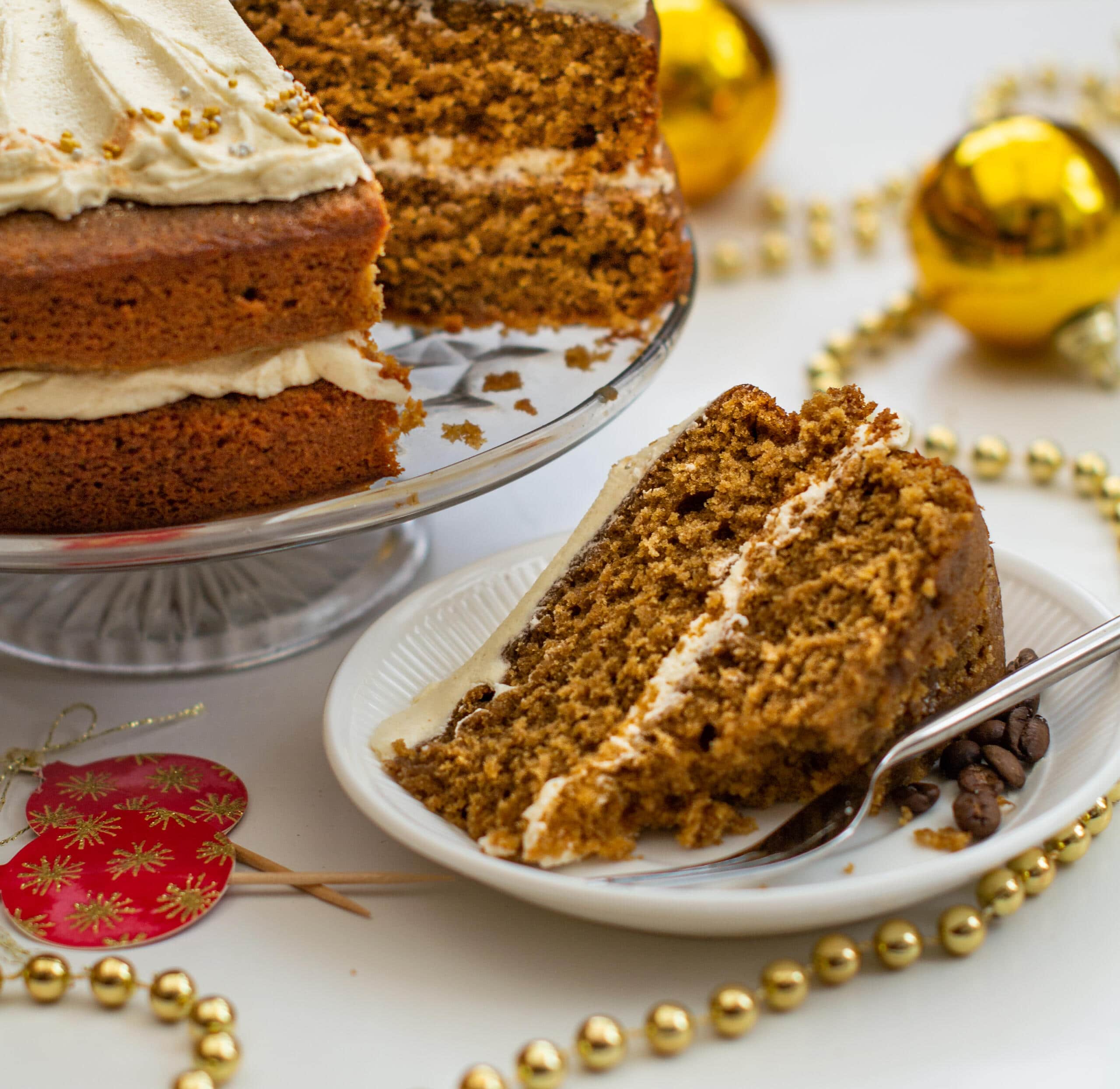 slice of ginger layer cake in front of whole cake surrounded by gold beads and red cake topper