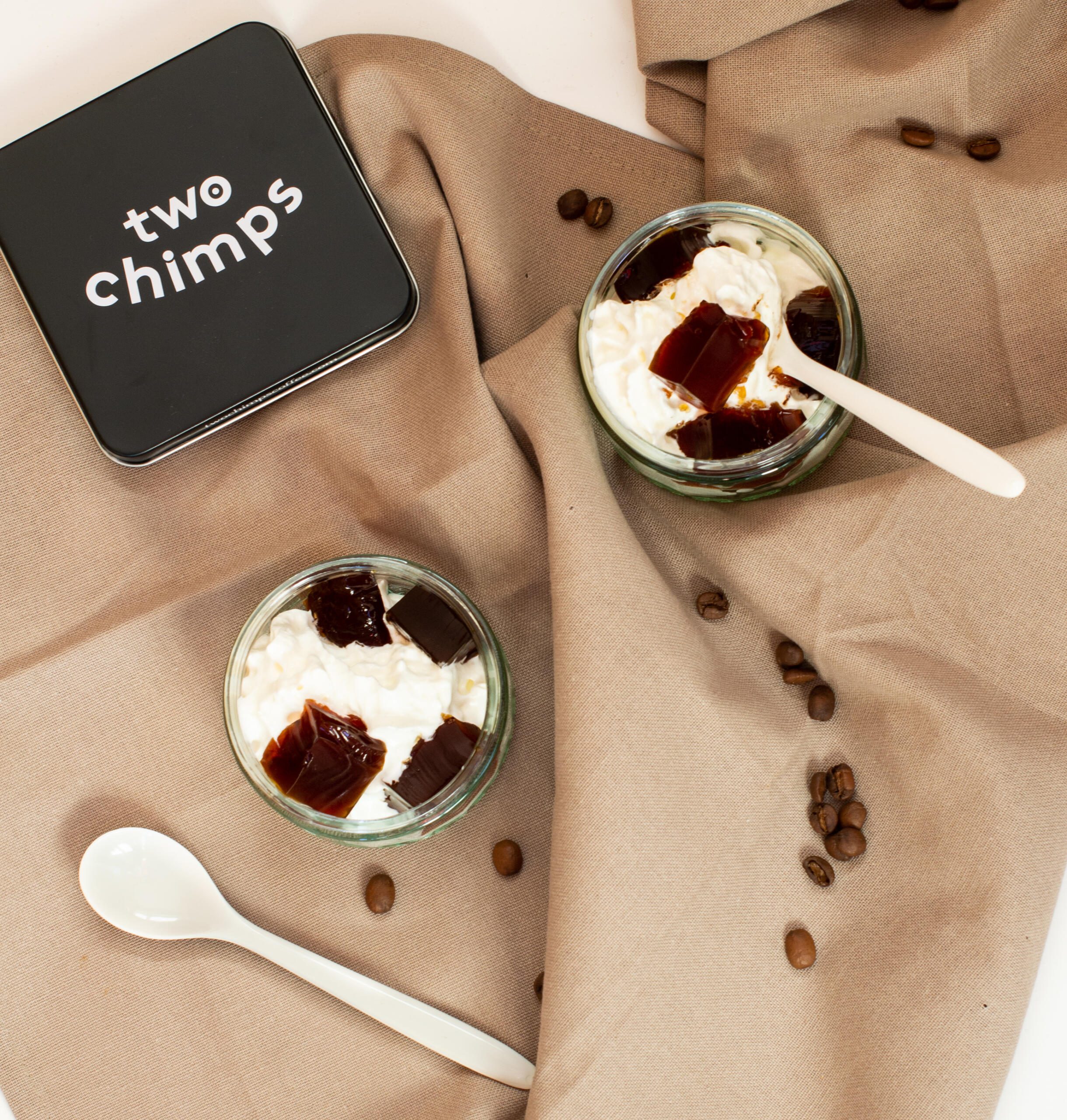 Two glass dishes of cream and coffee jelly cubes with white teaspoons and Two Chimps coffee tin lid