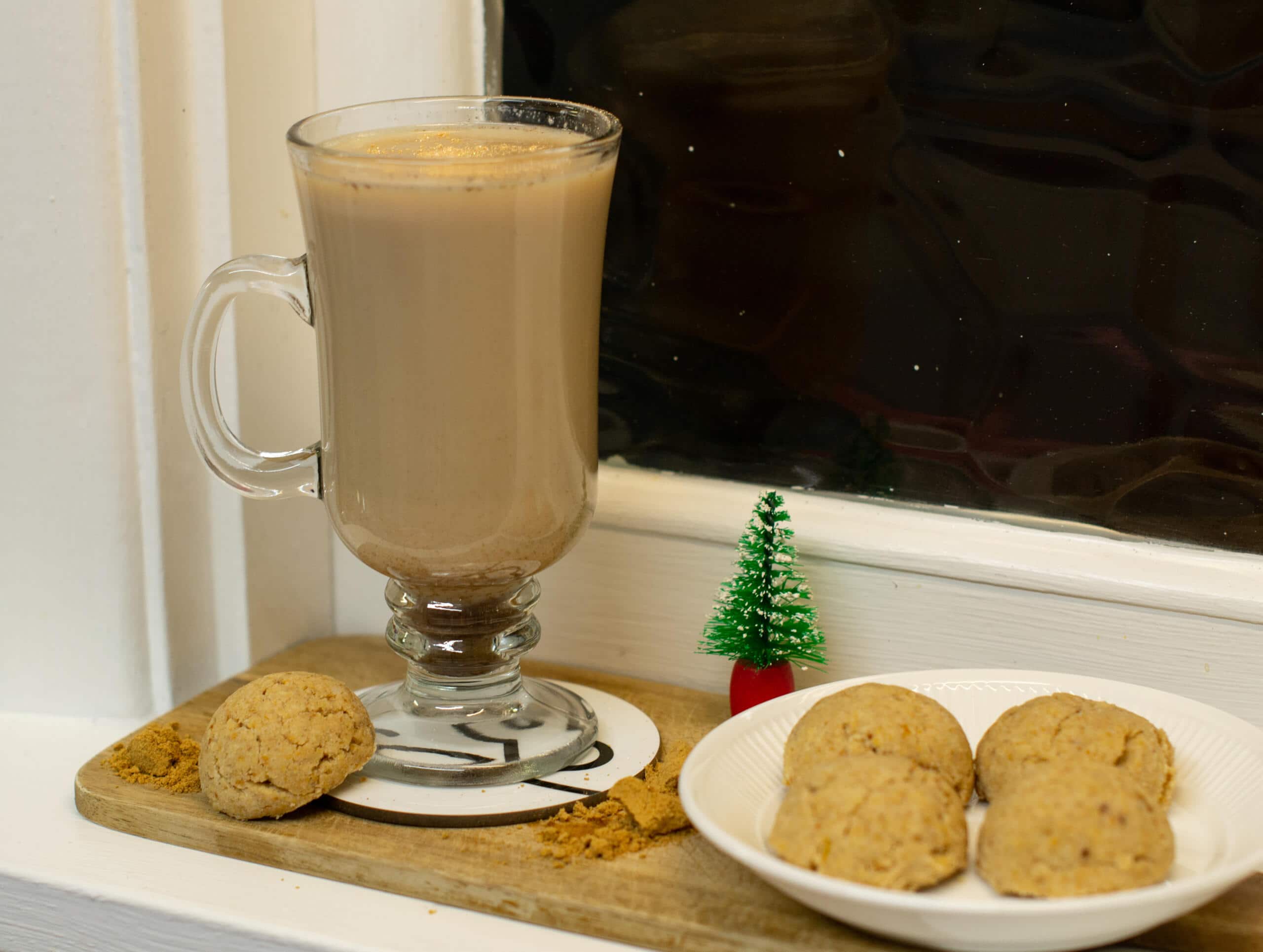 Gingerbread latte beside plate of cookies and mini Christmas tree