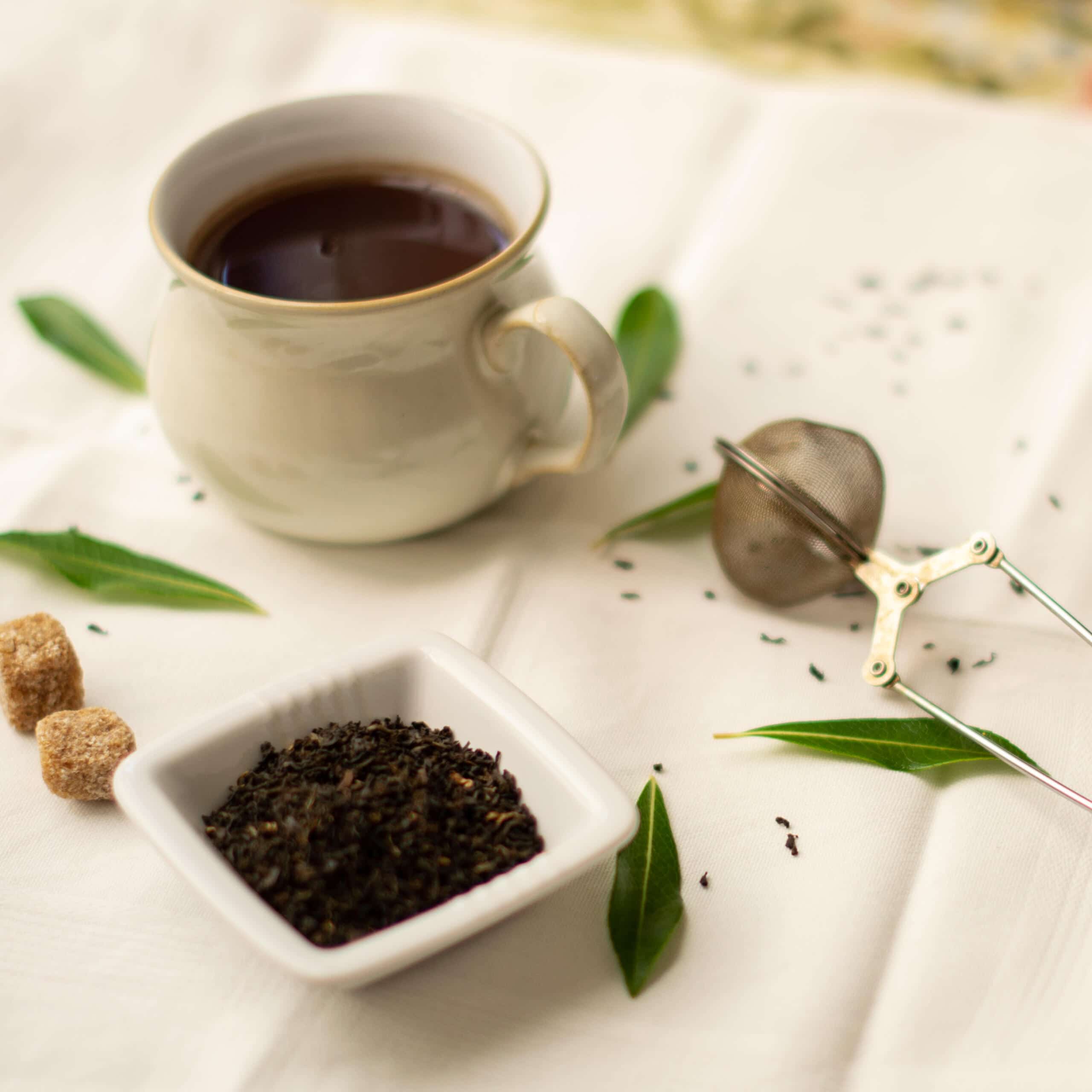 Tea cup with white dish of loose leaf Darjeeling, leaves and tea infuser 