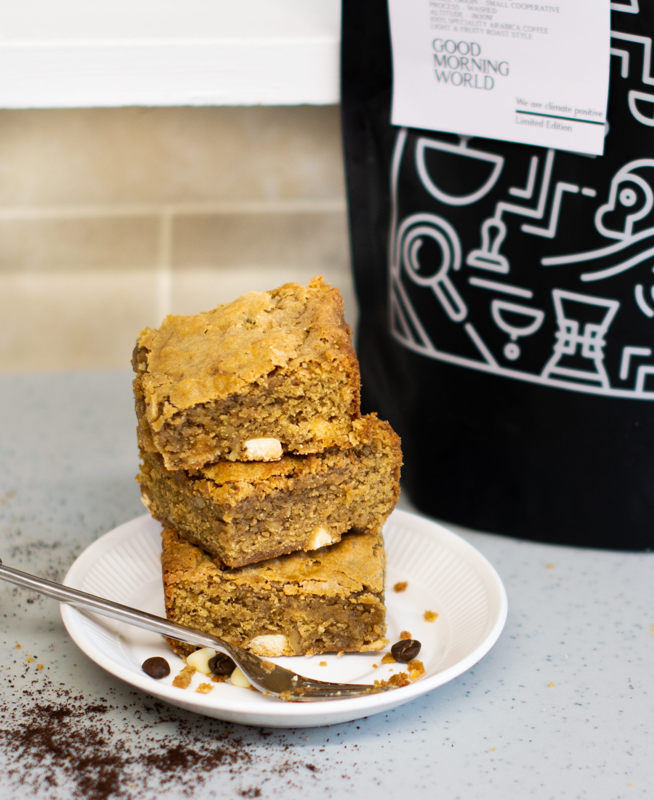 Stack of walnut blondies on a plate beside limited edition Two Chimps Coffee