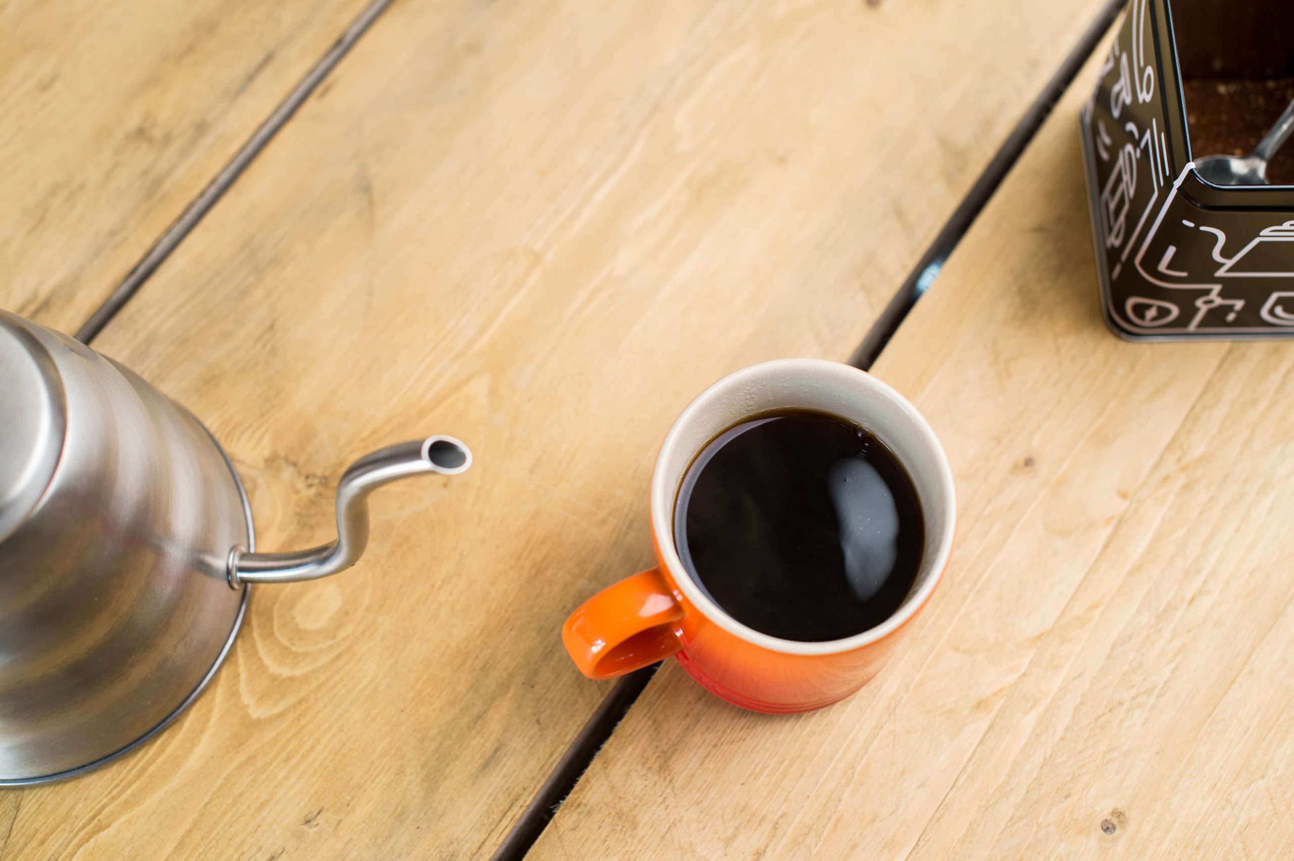 coffee in an orange mug with a kettle and tin