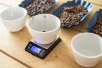 dropping coffee into a cupping bowl on a set of scales