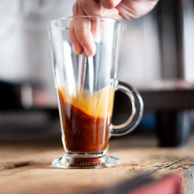 Stirring a shot of espresso in a tall coffee glass