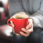 Someone in a grey jumper holding a red mug with coffee in