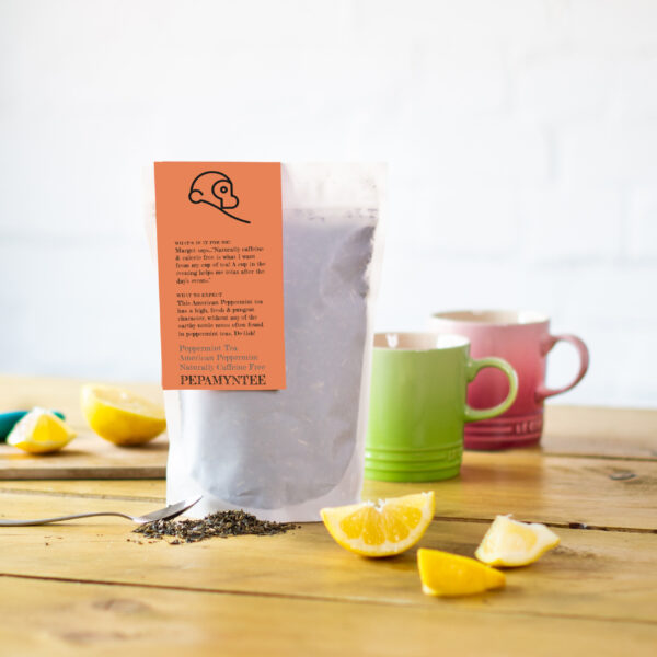 A pack of peppermint tea from Two Chimps on a table with slices of lemon and mugs