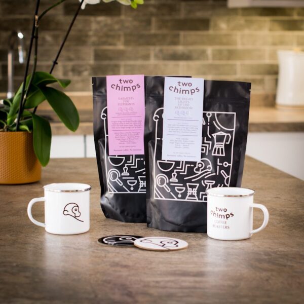 two bags of two chimps coffee with two mugs and two coasters on a kitchen worktop