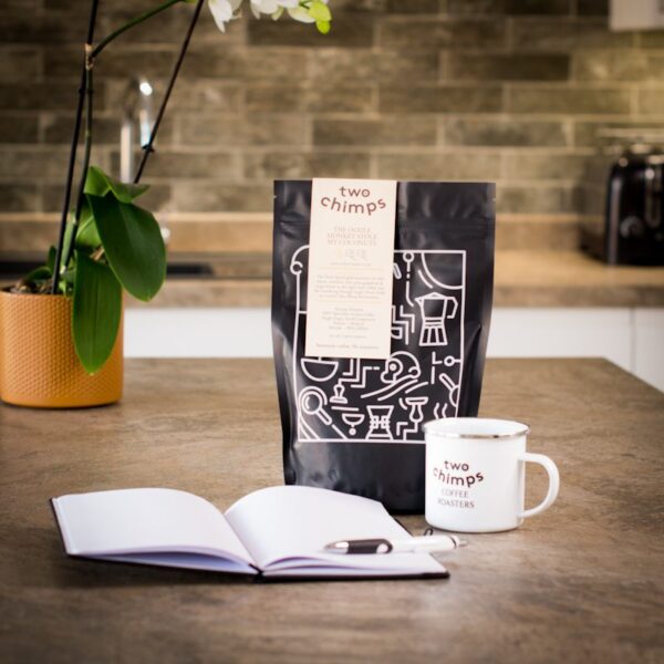 two chimps note book and pen with a mug and bag of coffee on a kitchen worktop