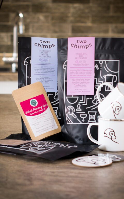 two bags of two chimps coffee,one bag of hot chocolate flakes,drinking spice,two enamel two chimps mugs and two chimp coasters all on a kitchen worktop