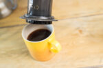 Close up of coffee in a yellow mug and AeroPress device