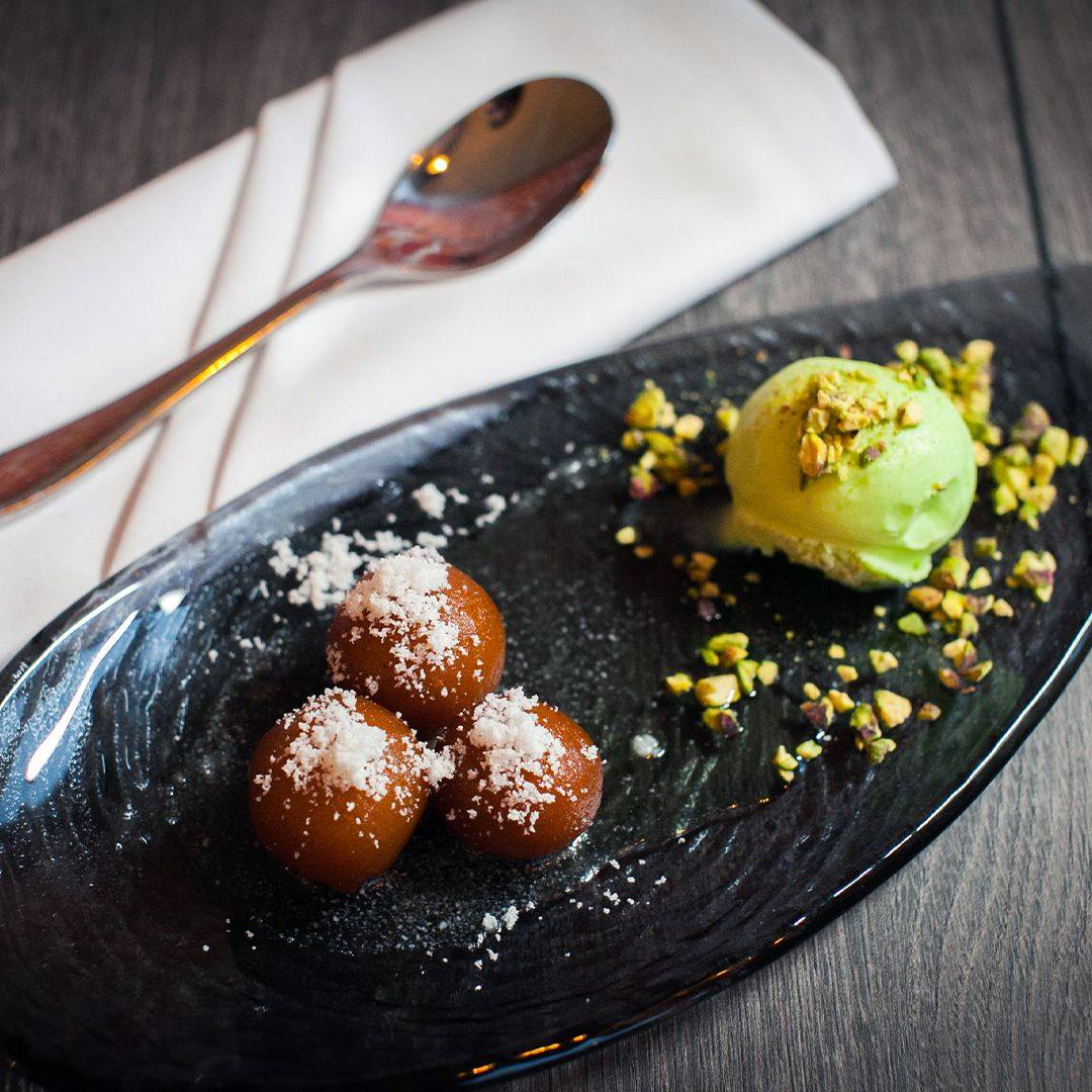 Coconut Gulab Jamun on a black plate with napkin and spoon