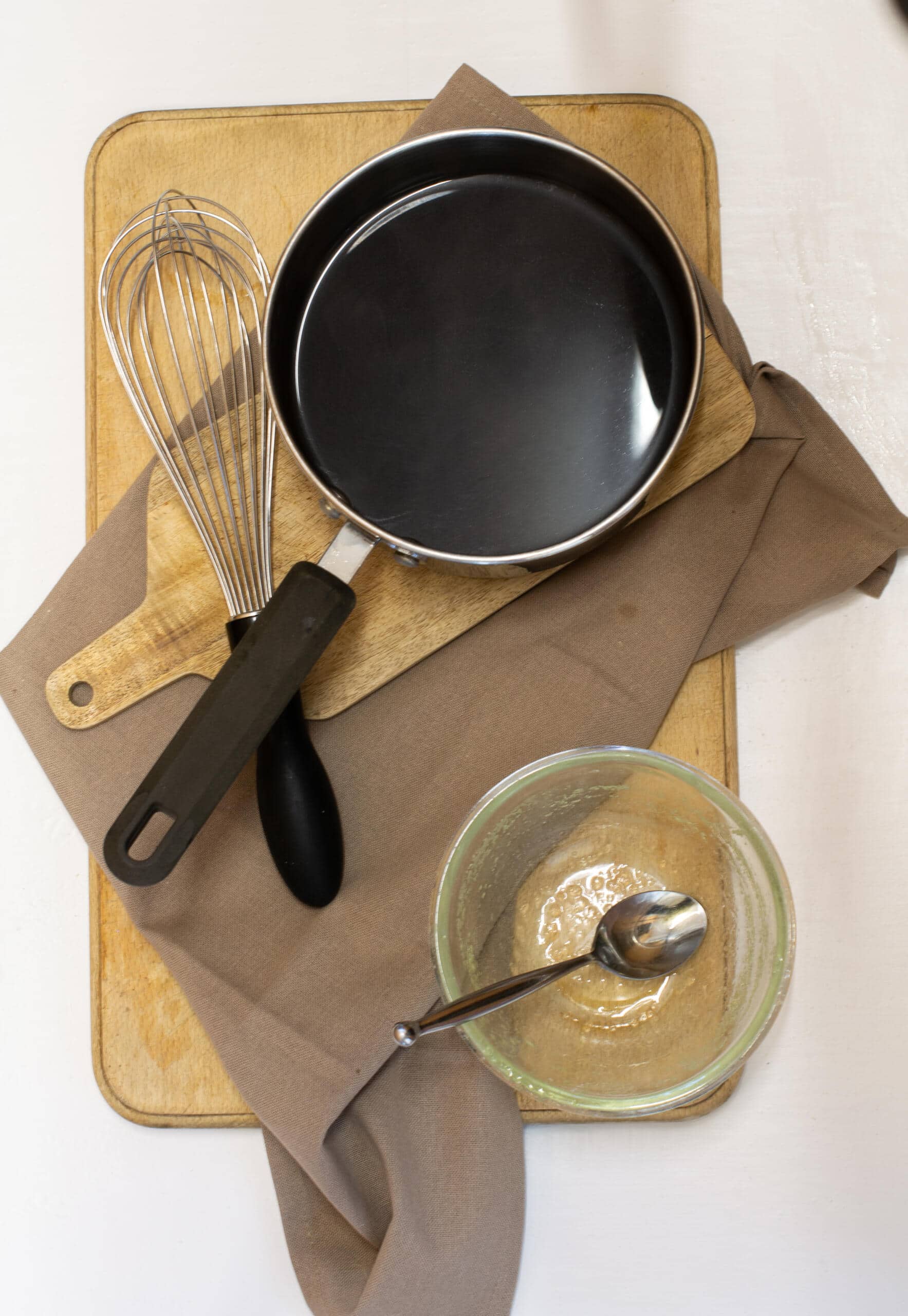 Coffee jelly mixture on saucepan besides metal whisk and a glass bowl with teaspoon in