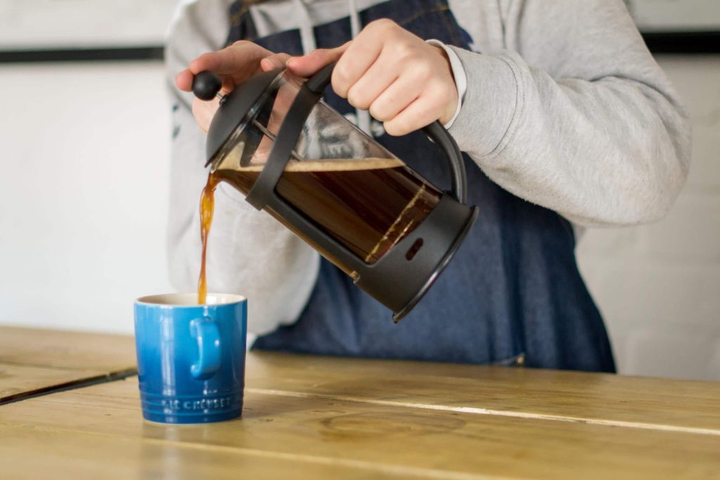 Pouring cafetiere coffee into a blue mug 