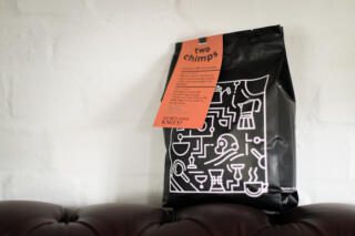 kilogram bag of Two Chimps Coffee sitting on red sofa before white brick wall