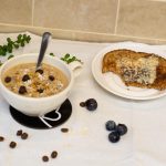 Bowl of coffee porridge beside blueberries and piece of toast and butter