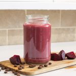 Beetroot latte glass on a chopping board with coffee beans and beetroot cubes