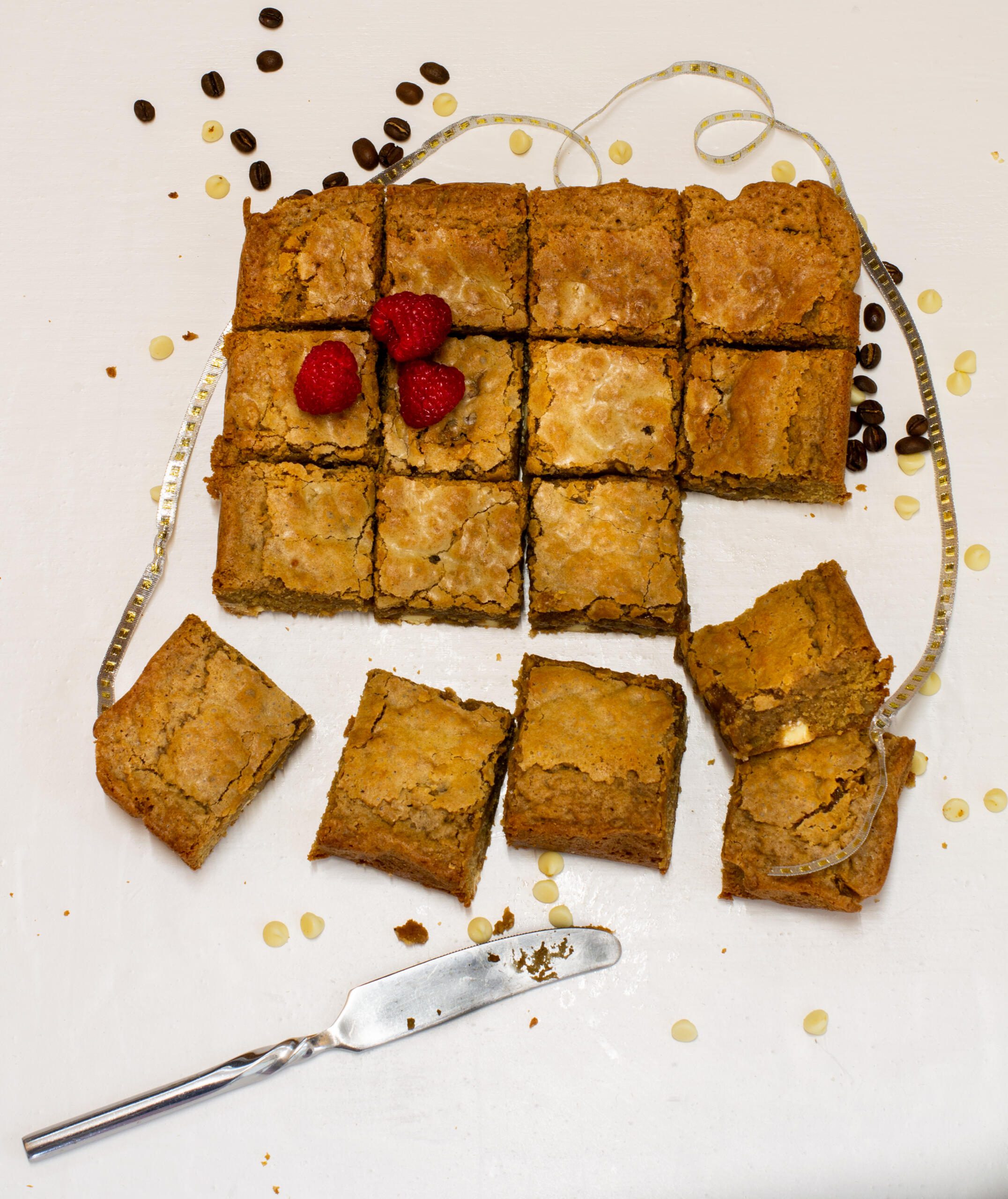 coffee blondies on a chopping board with knife, silver ribbon, coffee beans and raspberries 