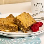 Two blondies on a plate with cake forks and raspberries
