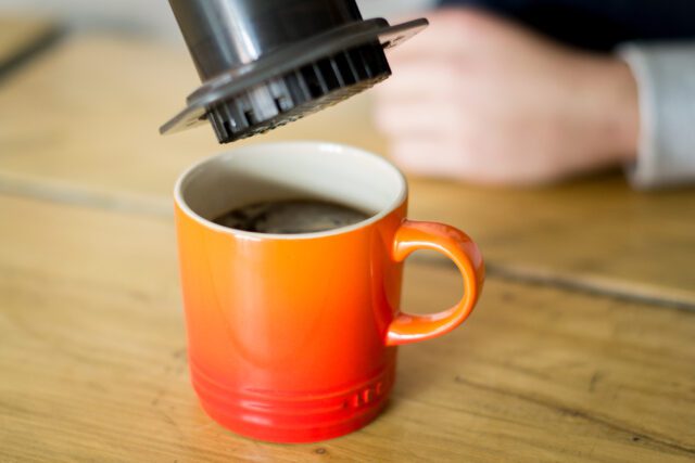 Lifting aeropress from coffee in an orange coffee mug 