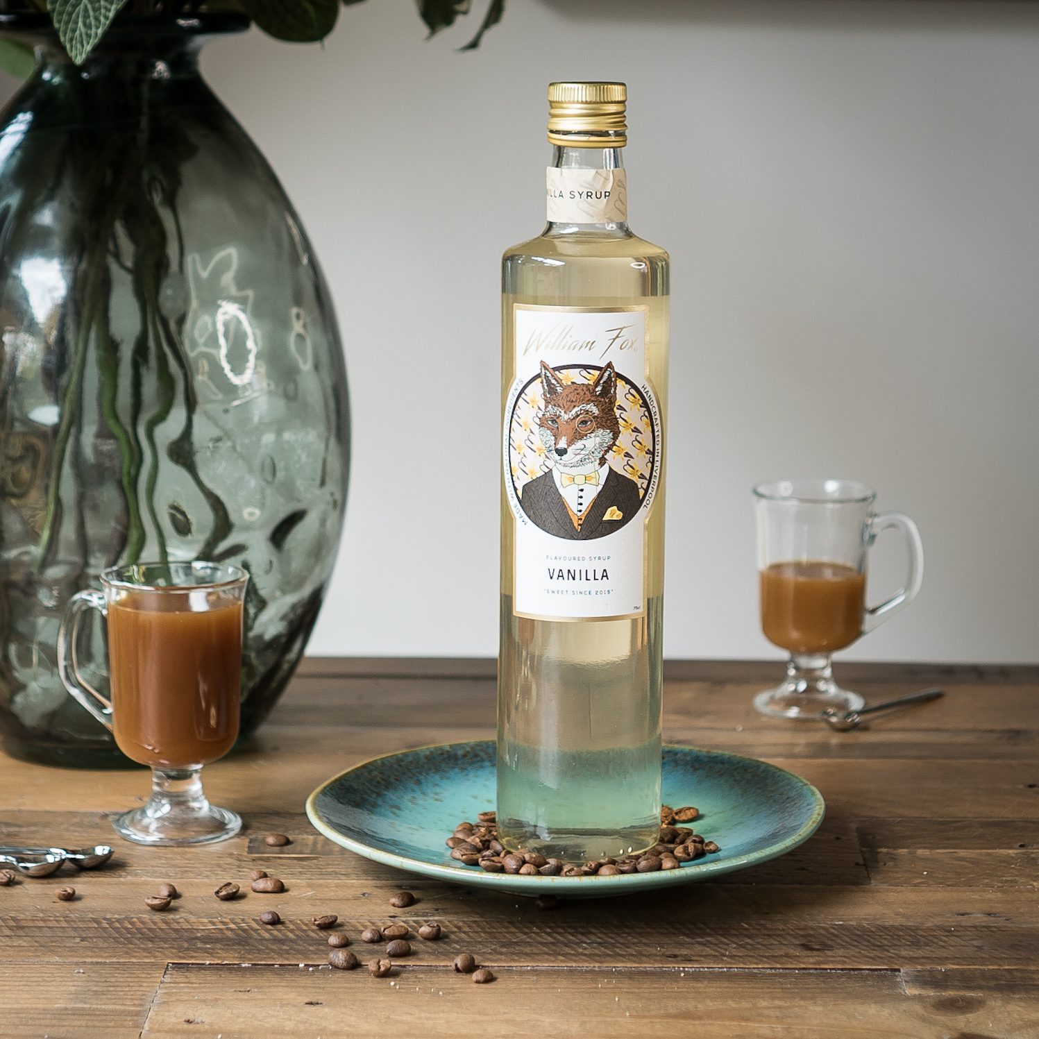 Bottle of coffee syrup on a blue plate with lattes in small glasses