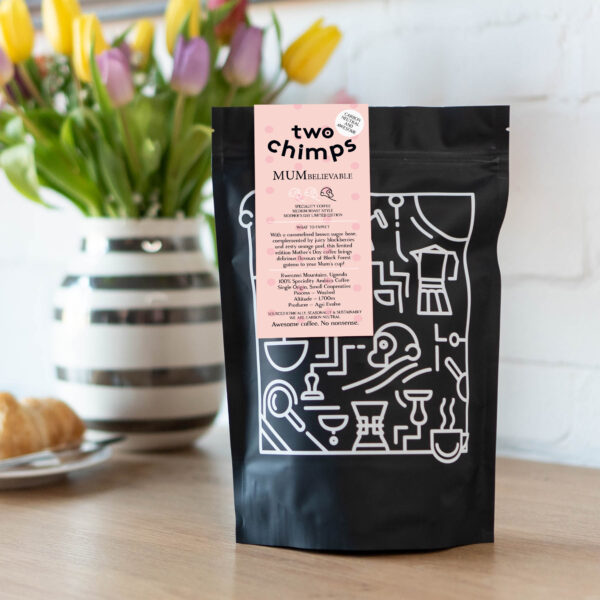 A bag of MUMbelievable Mother's Day coffee from Two Chimps on a table with a vase of flowers