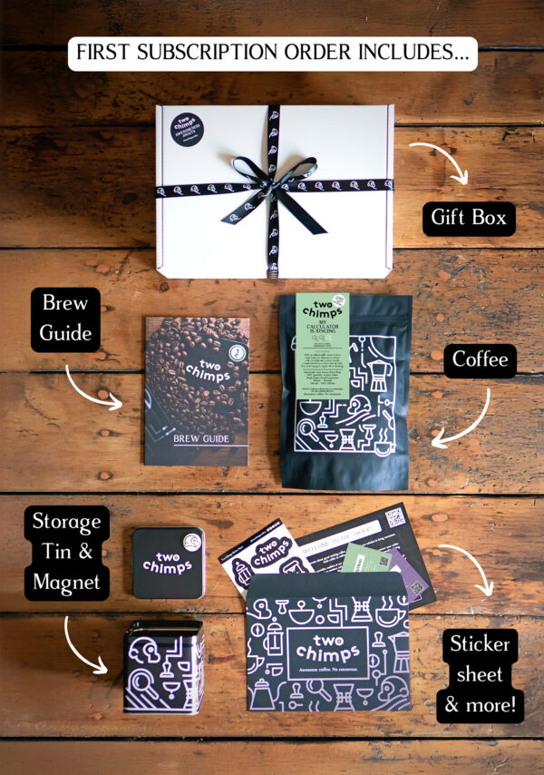 An image of a Two Chimps Coffee subscription box with the items included in it such as the brew guide, the storage tin & magnet and the coffee bag