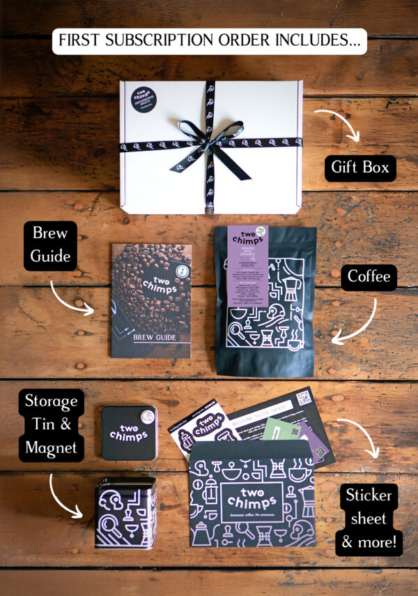 An image of a Two Chimps Coffee subscription box with the items included in it such as the brew guide, the storage tin & magnet and the coffee bag
