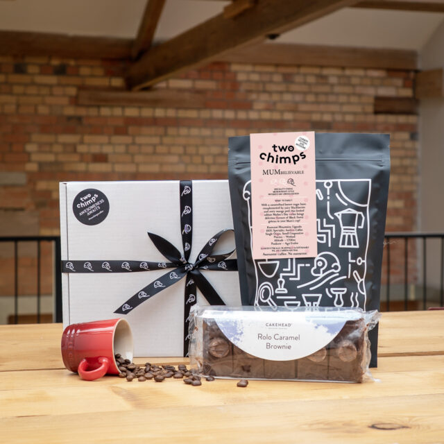 A Mother's Day coffee and cake gift box on a table with pack of brownies and bag of coffee, plus a mug of spilled coffee beans