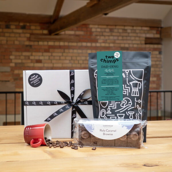 An image of the Two Chimps Father's Day coffee and cake gift set on a table with mug of spilled coffee beans