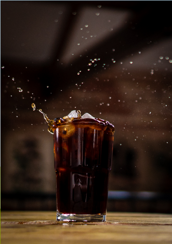 Ice falling into a glass of Two Chimps Cold Brew coffee creating a splash in the air and onto the table
