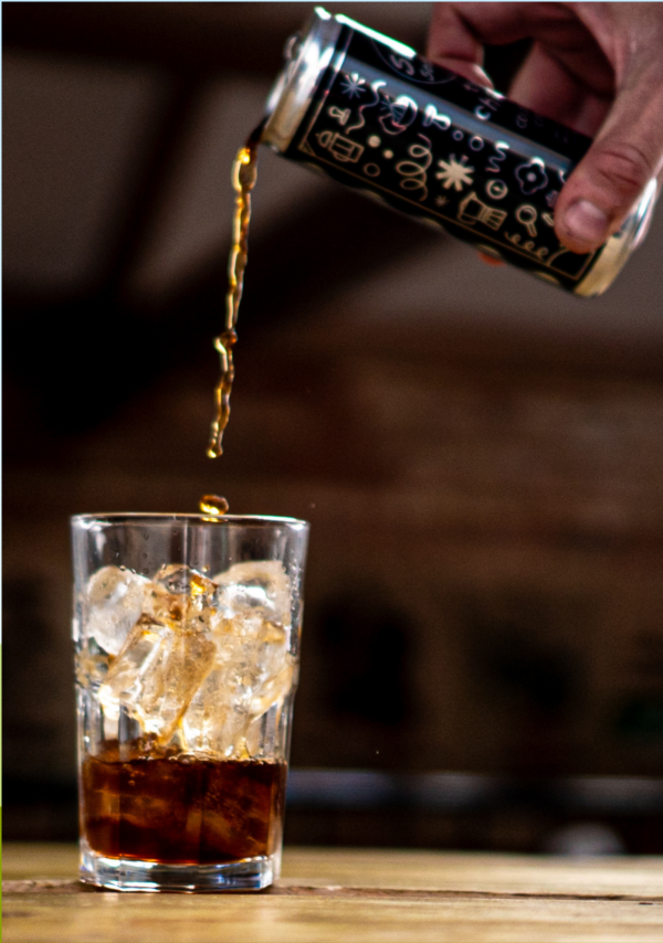 Pouring a can of Two Chimps Cold Brew coffee into a glass that is already half full, containing ice